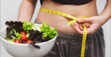 Foto del vientre de una mujer que rodea su vientre con una cinta métrica que practica una dieta para eliminar grasa abdominal en mujeres