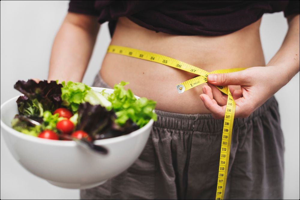 Foto del vientre de una mujer que rodea su vientre con una cinta métrica que practica una dieta para eliminar grasa abdominal en mujeres