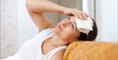 imagen de una mujer que sufre sofocos en la menopausia tendida en el sofá con una toalla en la cabeza