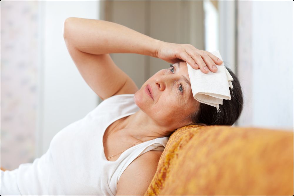 imagen de una mujer que sufre sofocos en la menopausia tendida en el sofá con una toalla en la cabeza