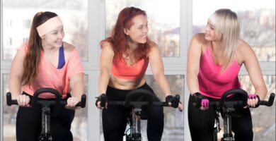 Foto de 3 mujeres sobre una bicicleta estática disfrutando de los beneficios psicológicos de hacer deporte