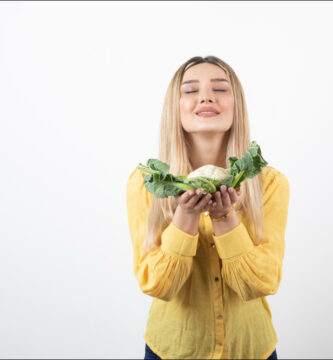 mujer joven rubia que sostiene una coliflor en sus manos y que representa los alimentos que bajan el azúcar