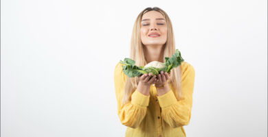 mujer joven rubia que sostiene una coliflor en sus manos y que representa los alimentos que bajan el azúcar