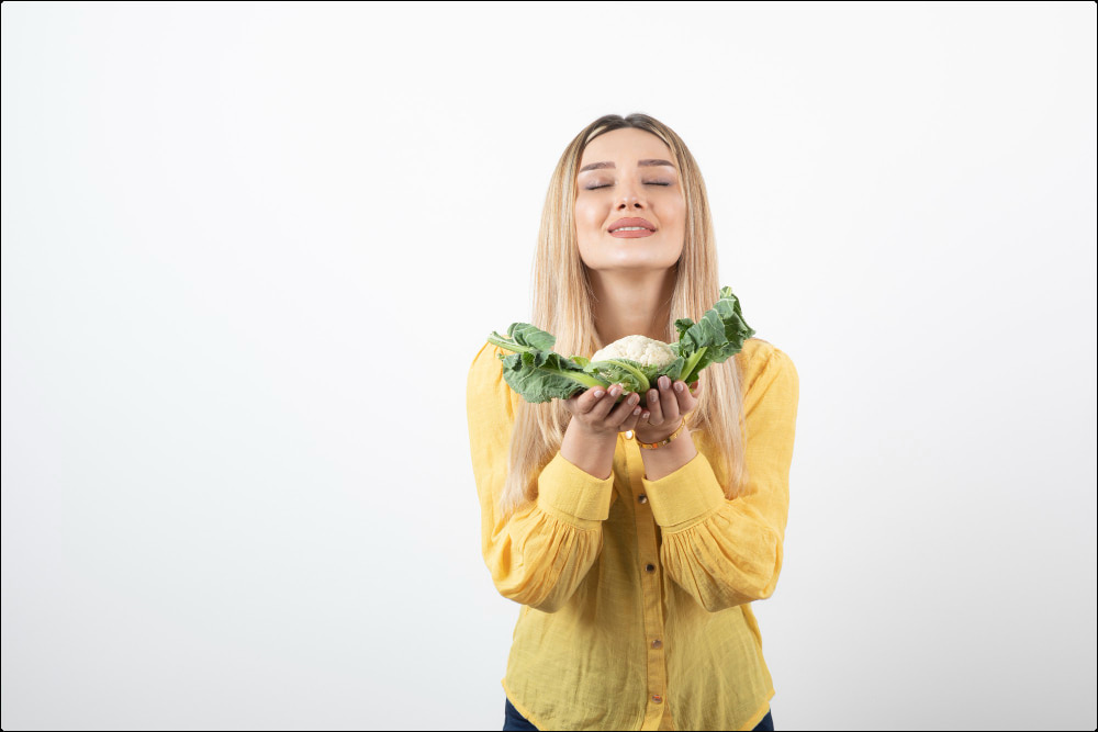 mujer joven rubia que sostiene una coliflor en sus manos y que representa los alimentos que bajan el azúcar