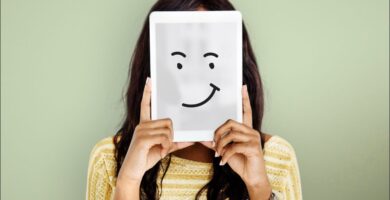 mujer tapándose la cara con una cartulina con una carita soriente, que simboliza la importancia de saber cómo controlar las emociones