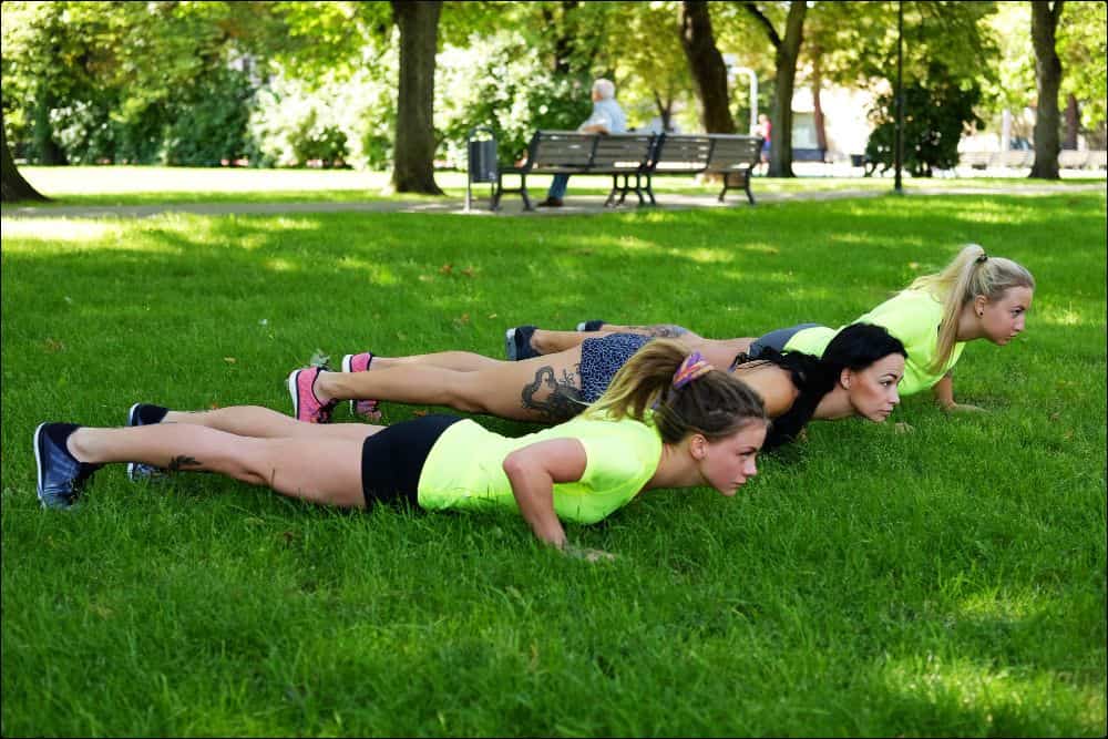 foto de 3 mujeres haciendo flexiones en el césped como parte de sus entrenamientos al aire libre