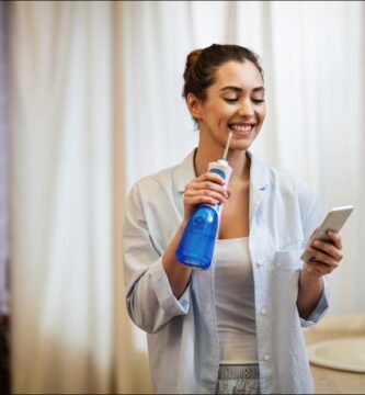 foto de mujer usando un irrigador bucal mientras mira su teléfono