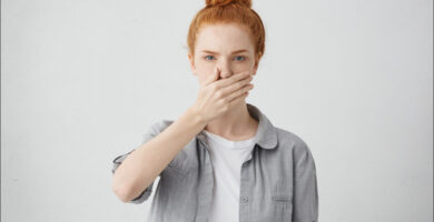 foto de una mujer pelirroja con mal aliento mirando a cámara que se tapa la boca con la mano