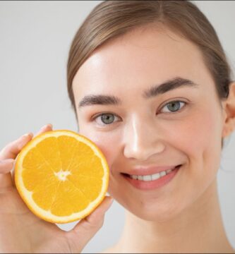 imagen de una mujer con una naranja uno de los alimentos con mayor proporción de vitamina c, algo que es bueno para la piel