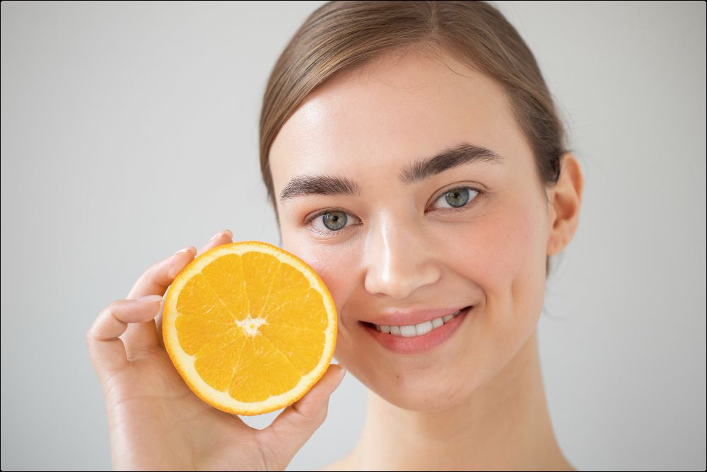 imagen de una mujer con una naranja uno de los alimentos con mayor proporción de vitamina c, algo que es bueno para la piel